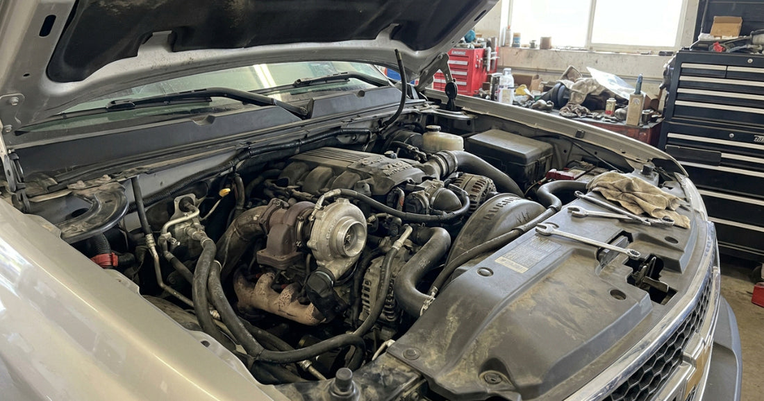 Open engine bay of a silver truck in a workshop, showing a turbocharger, with wrenches resting on the radiator cover.