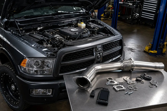 6.7 Cummins engine bay with diesel delete kit components including 5-inch DPF delete pipe, EGR block-off plates, and delete tuner on workbench