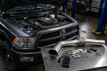 6.7 Cummins engine bay with diesel delete kit components including 5-inch DPF delete pipe, EGR block-off plates, and delete tuner on workbench